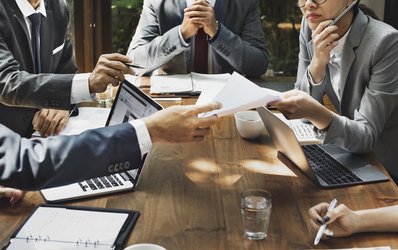 Business men and women around a table looking at laptops and papers