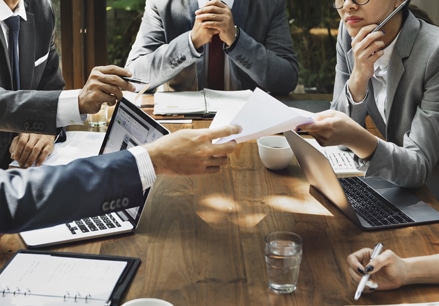 Business men and women around a table looking at laptops and papers